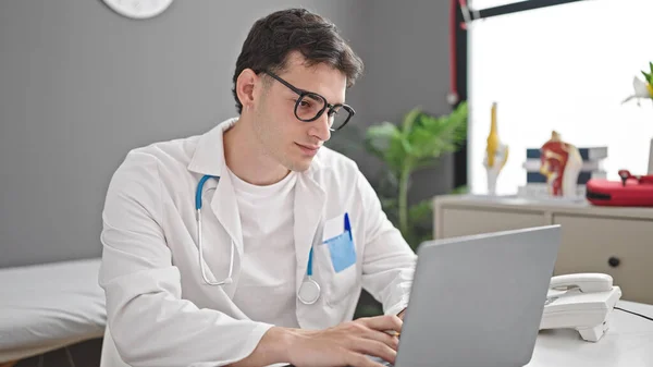 Young Hispanic Man Doctor Using Laptop Working Clinic — стоковое фото