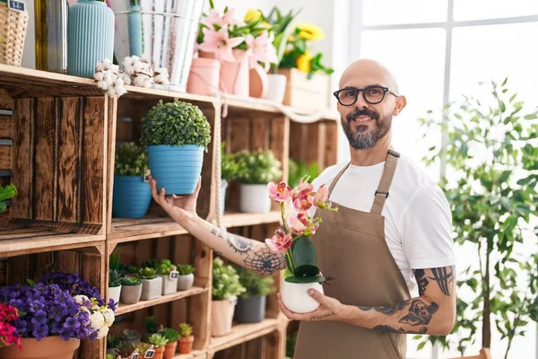 Young bald man florist smiling confident holding plants at florist