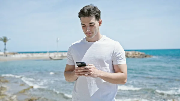 Joven Hombre Hispano Sonriendo Confiado Usando Smartphone Playa —  Fotos de Stock