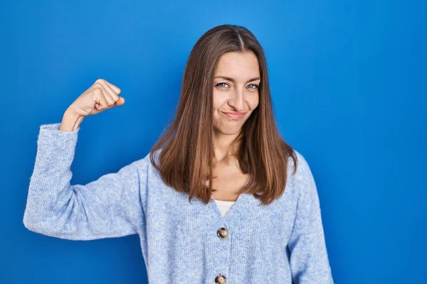 Young Woman Standing Blue Background Strong Person Showing Arm Muscle — Zdjęcie stockowe