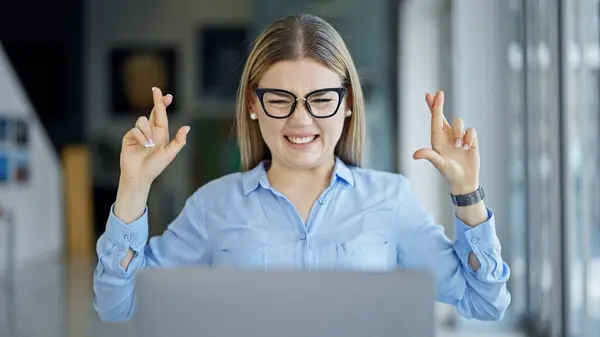 Young blonde woman business worker using laptop crossing finger for lucky at office