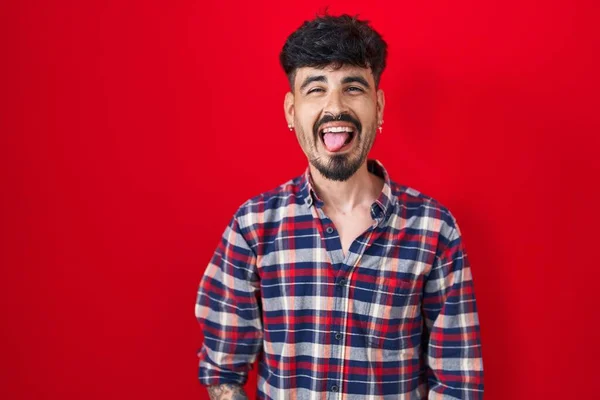 Homem Hispânico Jovem Com Barba Sobre Fundo Vermelho Furando Língua — Fotografia de Stock