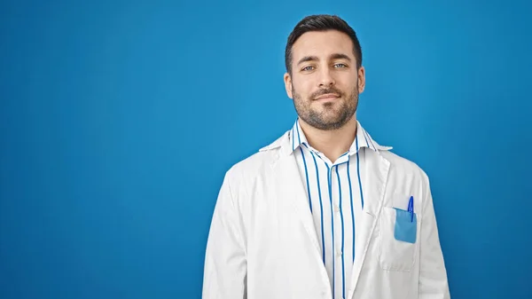 Joven Médico Hispano Sonriendo Confiado Pie Sobre Fondo Azul Aislado —  Fotos de Stock