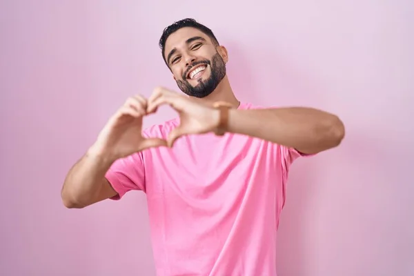 Spaanse Jongeman Staat Roze Achtergrond Glimlachend Liefde Doen Hart Symbool — Stockfoto
