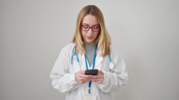 Νεαρή Ξανθιά Γυναίκα Γιατρός Χαμογελά Χρησιμοποιώντας Smartphone Πάνω Από Απομονωμένο — Αρχείο Βίντεο