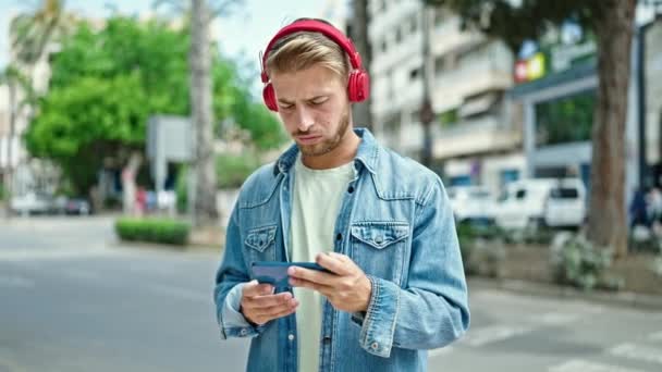 年轻的高加索人头戴耳机 头戴智能手机在街上观看足球比赛 — 图库视频影像
