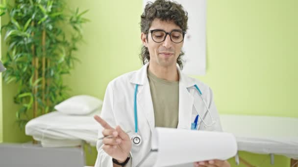 Young Hispanic Man Doctor Writing Medical Report Speaking Clinic — Stock Video