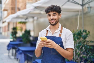 Restoranda çalışan akıllı telefonu kullanan genç bir Arap garson.