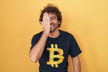 İspanyol asıllı genç adam bitcoin t-shirt giyiyordu. Bir gözünü eliyle kapatıyordu. Yüzünde kendine güvenen bir gülümseme ve sürpriz bir duygu vardı.. 