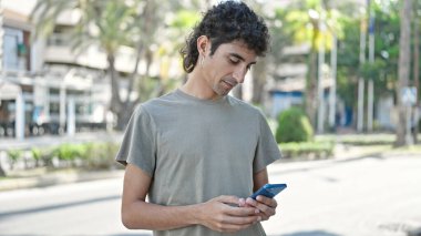 Genç İspanyol adam akıllı telefon kullanıyor. Sokakta ciddi bir ifadesi var.