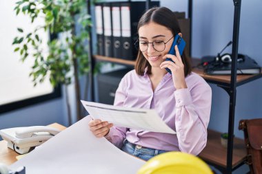 Genç İspanyol kadın mimar ofisteki akıllı telefon okuma belgesiyle konuşuyor.