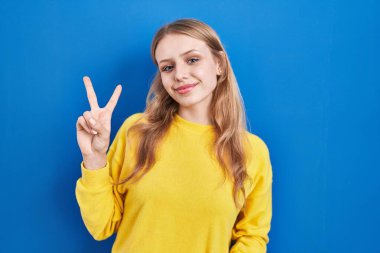 Young caucasian woman standing over blue background showing and pointing up with fingers number two while smiling confident and happy. 