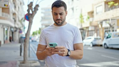 Genç İspanyol adam akıllı telefon kullanıyor. Sokakta ciddi bir ifadesi var.