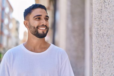 Genç Arap adam gülümsüyor. Kendinden emin. Caddenin kenarına bakıyor.