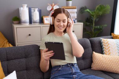 Young beautiful woman listening to music sitting on sofa at home