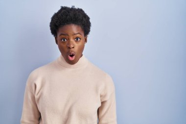 Mavi arka planda dikilen Afro-Amerikalı kadın şaşkınlık, korku ve heyecan dolu bir yüz ifadesiyle dehşete düşmüş ve şok olmuştu.. 