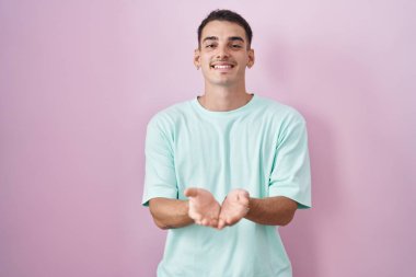 Pembe arka planda duran yakışıklı İspanyol adam avuçlarını birbirine uzatarak gülümsüyor ya da el hareketi yapıyor. Bekleme ve koruma 