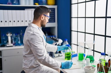 Laboratuardaki belgeye mikroskop kullanarak bilim adamı üniforması giyen İspanyol genç adam.