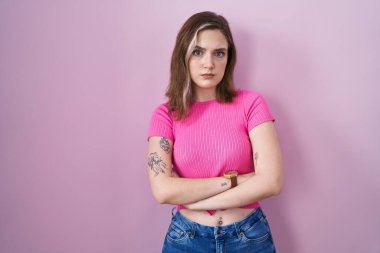 Blonde caucasian woman standing over pink background skeptic and nervous, disapproving expression on face with crossed arms. negative person. 