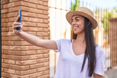 Young hispanic woman tourist smiling confident making selfie by the smartphone at street