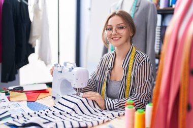Terzide dikiş makinesi kullanan kendine güvenen genç sarışın kadın terzi.