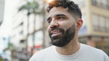Young hispanic man smiling confident looking to the side at street