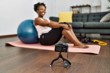 Afrikalı Amerikalı bir kadın evdeki yoga minderinde oturup video kaydediyor.