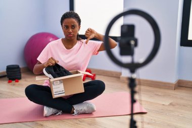 Örgülü genç Afro-Amerikalı, spor salonunda akıllı telefonlu vlog dersleri kaydediyor. Kızgın suratlı, olumsuz işaretli, baş parmakları aşağıda, reddedilme konsepti var. 