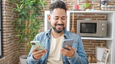 Yemek odasındaki masada oturan akıllı telefon kullanan genç latin adam.