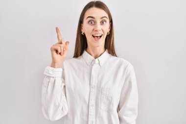 Young caucasian woman standing over isolated background pointing finger up with successful idea. exited and happy. number one. 