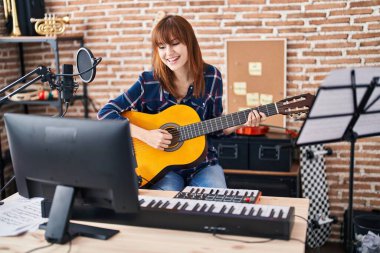 Genç bayan müzisyen müzik stüdyosunda klasik gitar çalarak şarkı söylüyor.