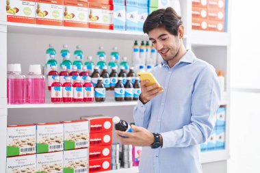 Young hispanic man customer make photo by smartphone to medicine bottle at pharmacy