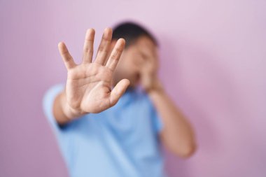 İspanyol adam pembe arka planda duruyor. Gözleri ellerle kaplıyor ve üzgün ve korku ifadeleriyle jestler yapıyor. utangaç ve olumsuz kavram. 