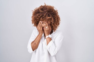 Beyaz arka planda duran kıvırcık saçlı genç İspanyol kadın yorgunluk ve baş ağrısı için gözlerini ovuşturuyor, uykulu ve yorgun ifade. görme sorunu 