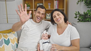 Üç kişilik aile evdeki kanepede el sallıyor.