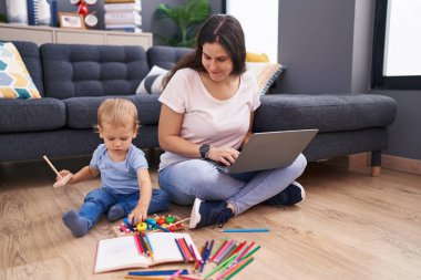 Anne ve oğlu dizüstü bilgisayar kullanıyor ve evde yerde oturuyor.