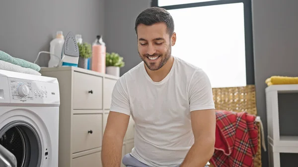 Çamaşır Odasında Yerde Oturmuş Kendinden Emin Gülümseyen Spanyol Genç Adam — Stok fotoğraf