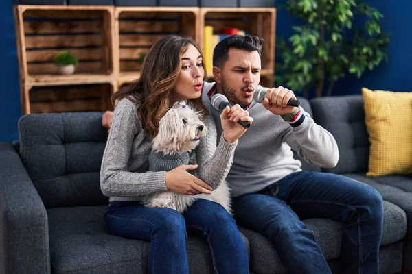 Man and woman singing song sitting on sofa with dog at home