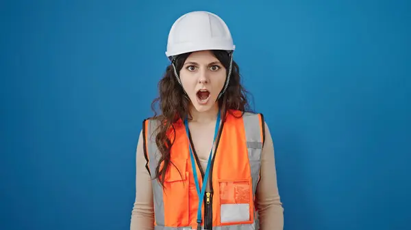 惊慌失措的女建筑工人站在孤立的蓝色背景下 脸上露出惊讶的表情 — 图库照片