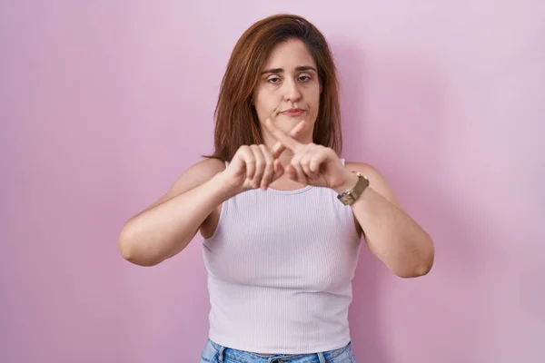 布鲁内特女人站在粉红的背景下 用手指交叉表示拒绝 做阴性手势 — 图库照片