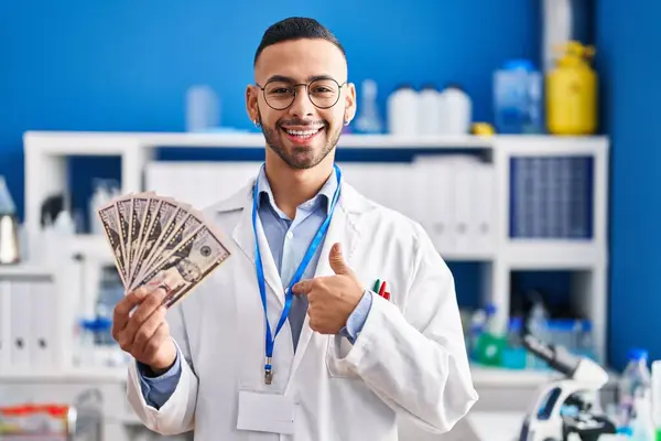 Young Hispanic Man Working Scientist Laboratory Holding Money Pointing Finger — ストック写真