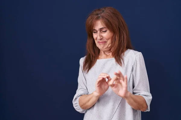Middle age woman standing over blue background disgusted expression, displeased and fearful doing disgust face because aversion reaction. with hands raised
