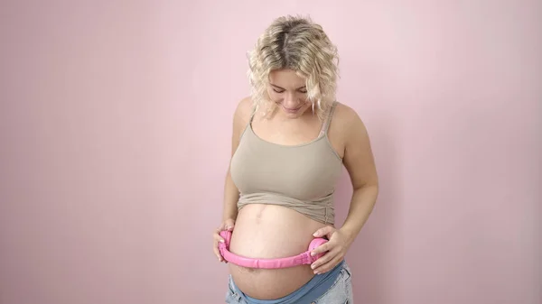 Jonge Zwangere Vrouw Glimlachen Zelfverzekerd Zetten Koptelefoon Buik Geïsoleerde Roze — Stockfoto