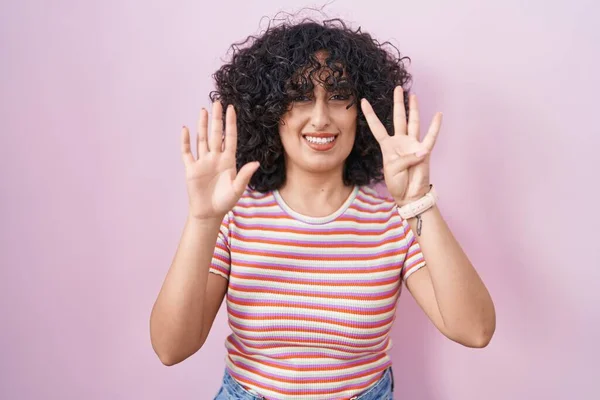 年轻的中东女人站在粉红的背景上 用9号手指指指指点点 自信而快乐地微笑着 — 图库照片