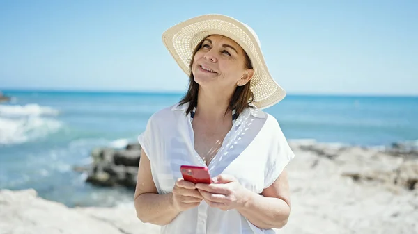 中年惊慌失措的女性游客在海滩上用智能手机微笑 — 图库照片