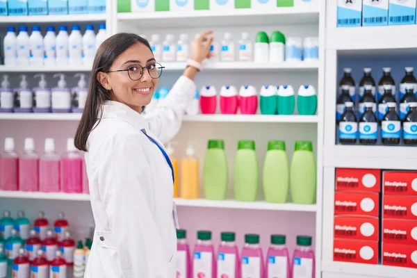 年轻美丽的惊慌失措的女药剂师微笑着 自信地将产品放在药店的架子上 — 图库照片