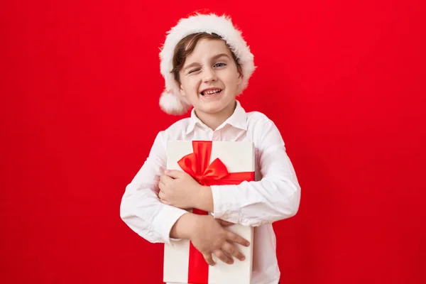 Little Caucasian Boy Wearing Christmas Hat Holding Gifts Winking Looking — Stock Photo, Image