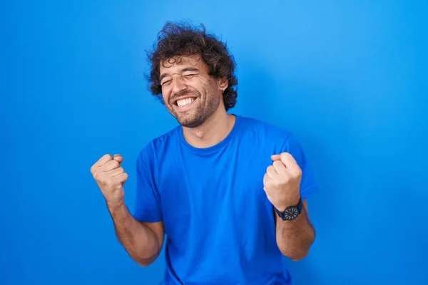 Латиноамериканец Стоящий Синем Фоне Счастлив Взволнован Делая Жест Победителя Поднятыми — стоковое фото