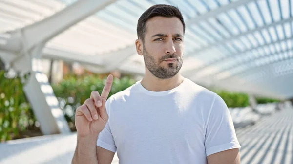 Young hispanic man standing with serious expression saying no with finger at park