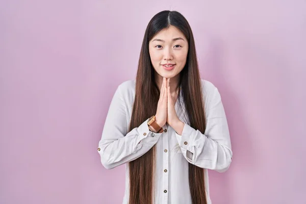 中国の若いです若いです女性の上に立ってピンクの背景一緒に手で祈って許しを求めて笑顔自信 — ストック写真